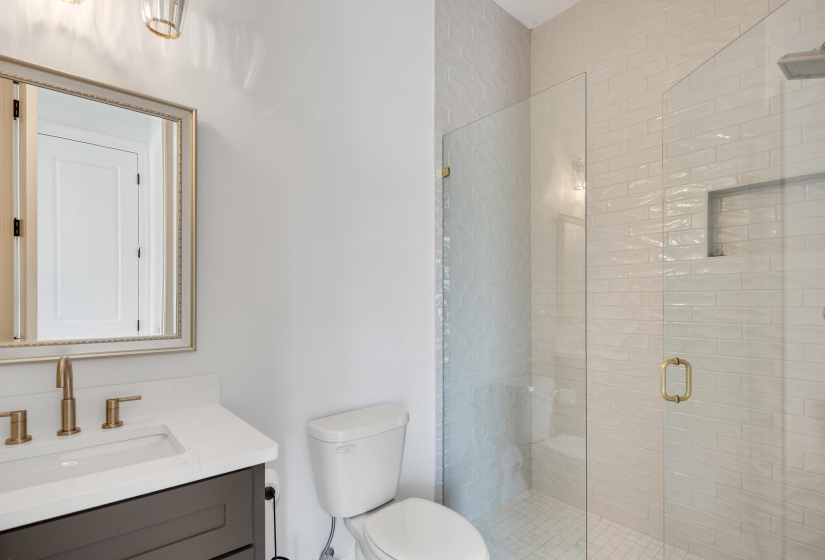 Bathroom featuring a frameless glass shower enclosure with a built-in niche, light-toned subway tile, a dark wood-finish vanity with a white countertop, and gold-finish fixtures