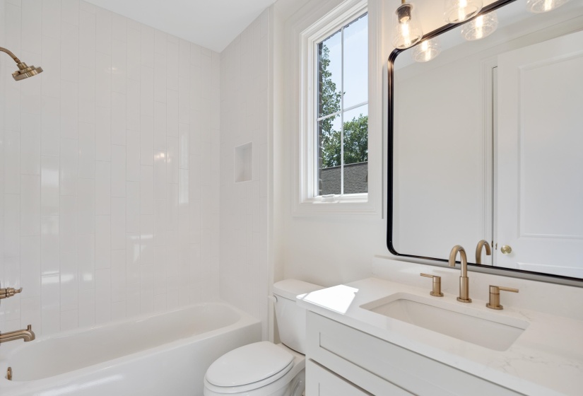 Bathroom featuring a tub/shower combination with white vertical subway tile, gold-tone fixtures, a built-in shower niche, and a vanity with a white countertop and integrated sink
