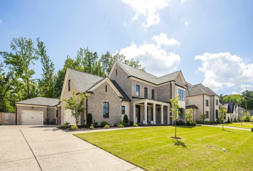 Architectural brick exterior with dark-framed windows, a covered front porch with white columns, and a detached garage