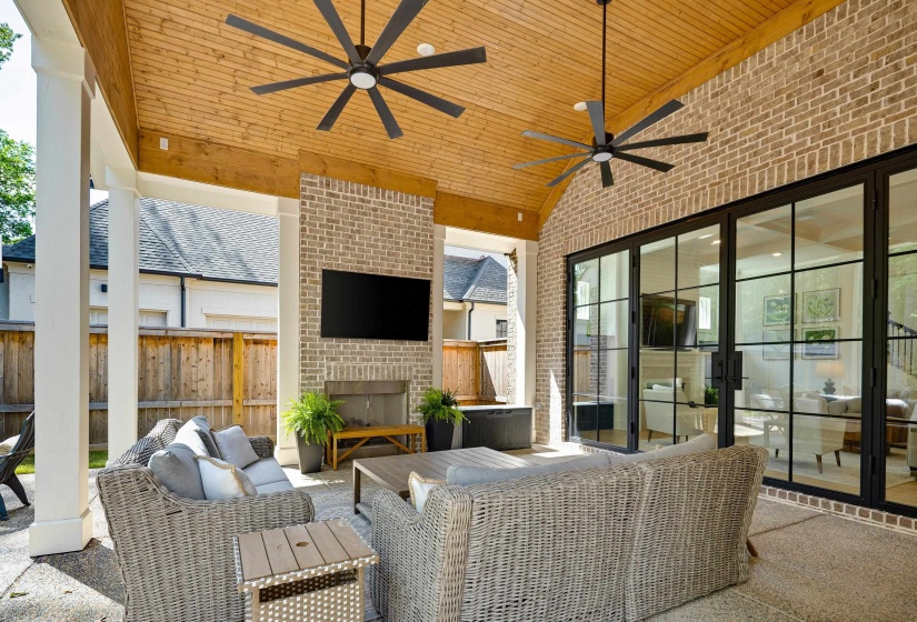 Covered outdoor living space featuring a brick accent wall, built-in fireplace, and a mounted television