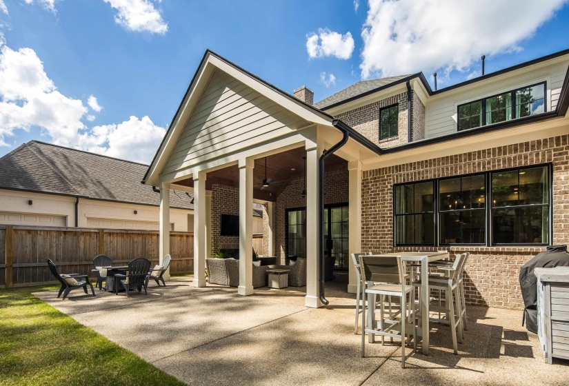 Expansive concrete patio offering a covered outdoor living area with a built-in fireplace, exposed brick accents, and a ceiling fan