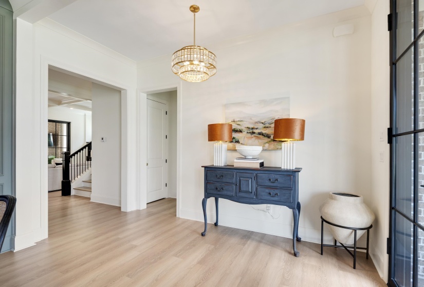 Bright entryway featuring light wood-finish flooring, a tiered chandelier, wide cased openings, a solid paneled door, and a black-framed glass door