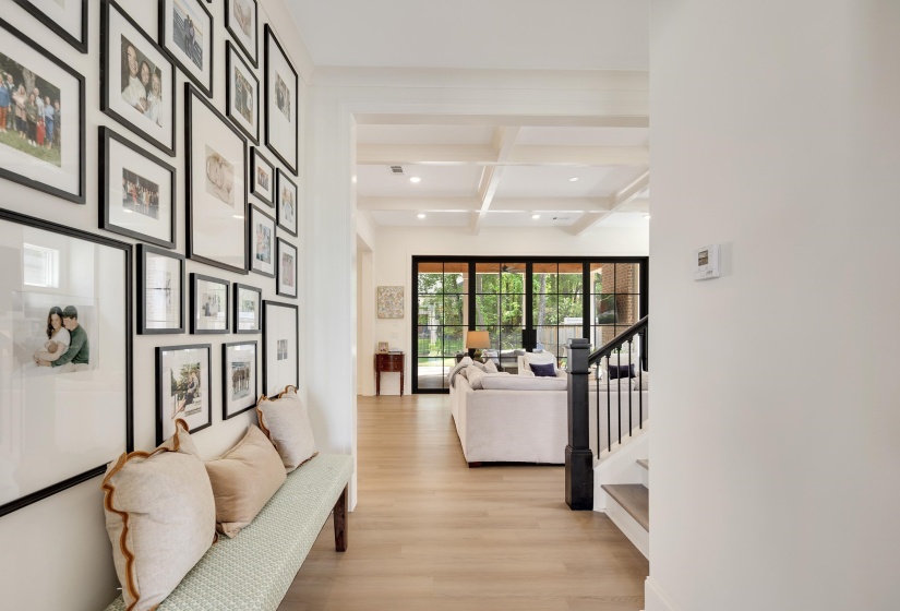 Open concept interior featuring light wood-finish flooring, a coffered ceiling, and a black wrought iron staircase railing