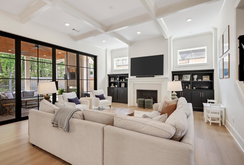 Spacious living area featuring coffered ceilings, light wood-finish flooring, and expansive black-framed glass doors opening to an outdoor patio