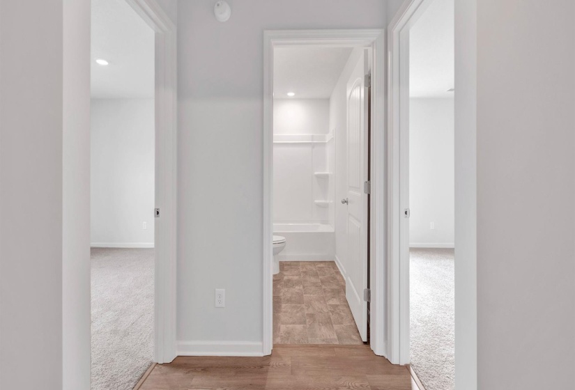 Hallway featuring wood-finish flooring leading to a bathroom with tiled flooring and a white tub/shower combination