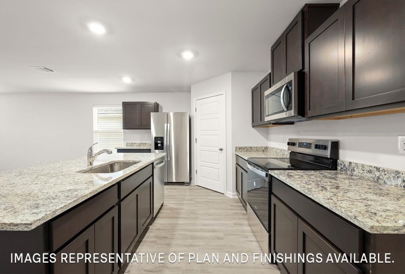 Kitchen with stainless steel appliances, a center island with sink, light wood-type flooring, light stone countertops, and dark brown cabinets