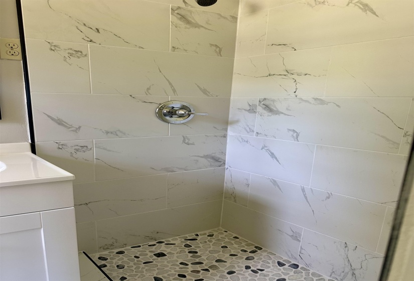 Shower stall featuring large format white and gray veined tile walls, a chrome shower control, and a river rock tile floor