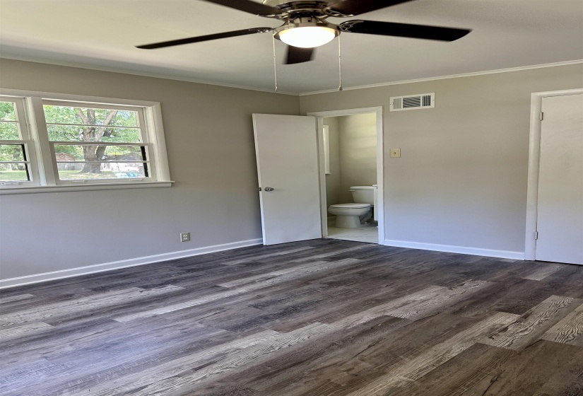 Spacious room featuring wood-finish flooring, a ceiling fan with integrated lighting, and multiple windows providing natural light