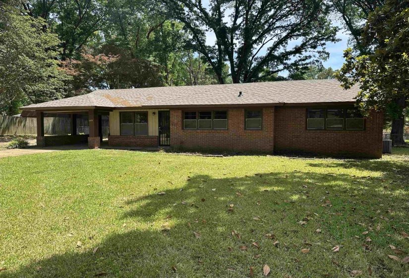 Brick exterior home featuring a covered carport, mature trees, and a spacious front lawn