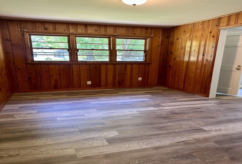 Room featuring wood paneling on walls, wood-finish flooring, and a triple window assembly