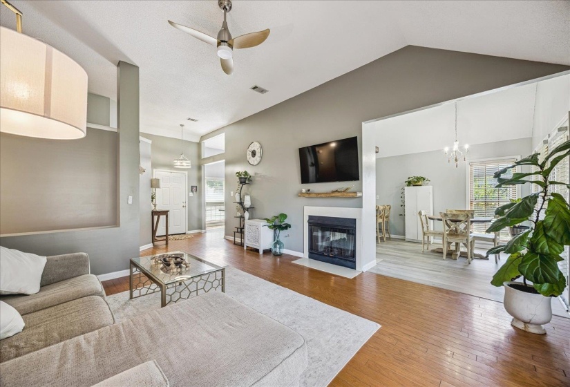 Vaulted ceilings featuring a ceiling fan, hardwood-finish flooring, and a fireplace with a mantel