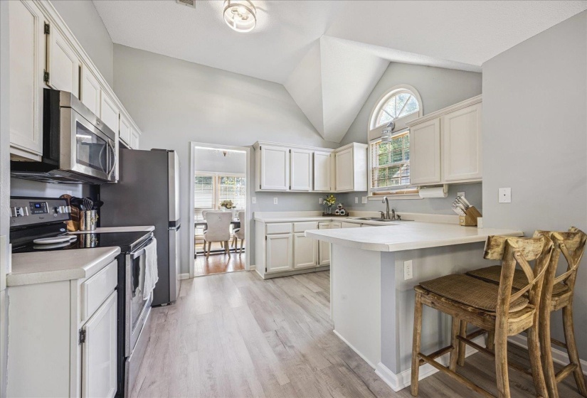 Light-filled kitchen featuring vaulted ceilings, wood-finish flooring, white cabinetry, a kitchen island with seating, and stainless steel appliances