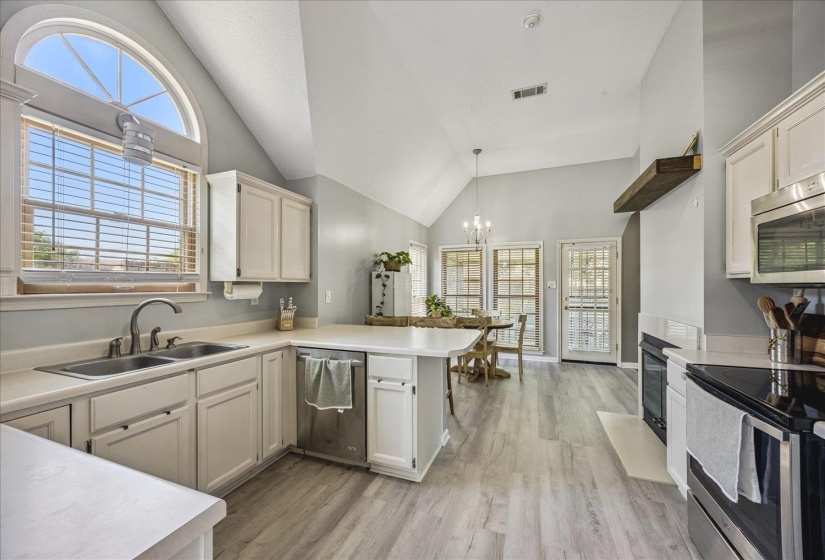 Vaulted ceiling kitchen featuring wood-finish flooring, white cabinetry, a double basin sink with a gooseneck faucet, and a breakfast bar