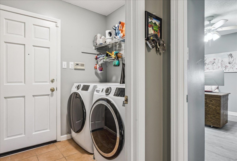 Dedicated laundry area featuring a white six-panel door, terracotta tile flooring, and integrated wire shelving for storage
