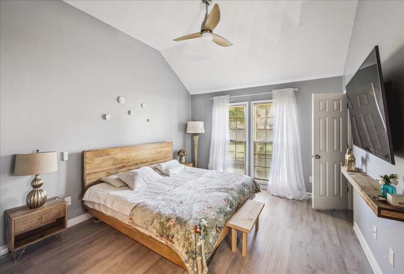 Vaulted ceiling bedroom featuring wood-finish flooring, a ceiling fan, and two windows with white sheer curtains