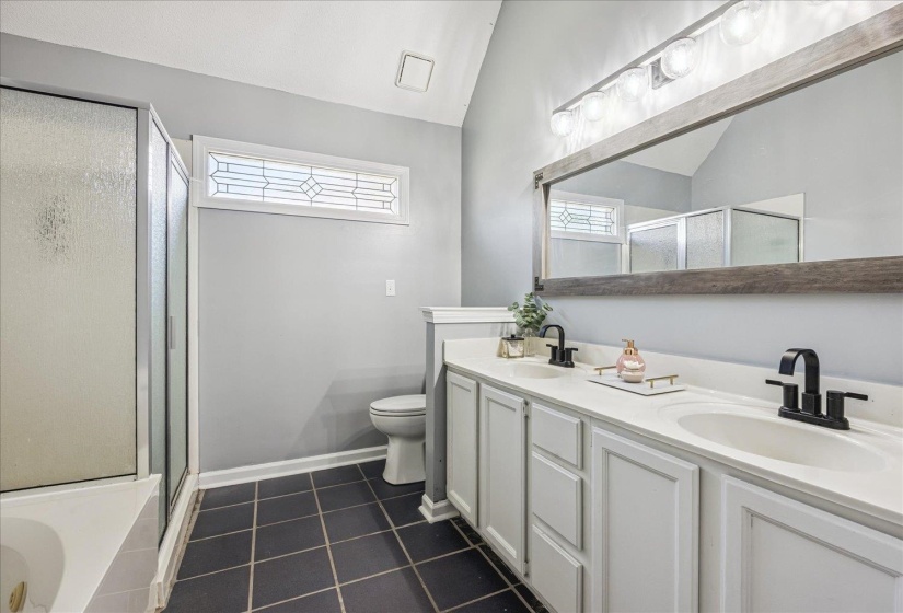 Bathroom featuring a dual vanity with white cabinetry and integrated sinks, matte black faucets, and a large wood-framed mirror