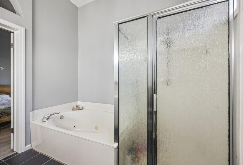 Bathroom featuring a white jetted soaking tub, chrome fixtures, and a shower enclosure with frosted glass panels and a metallic frame