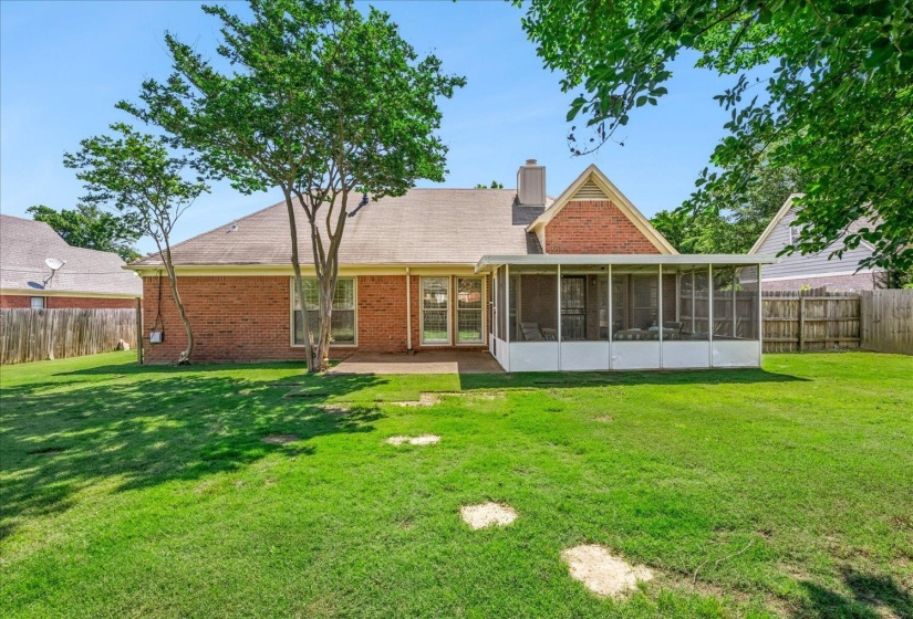 Brick exterior featuring a screened-in patio, concrete patio, and mature trees