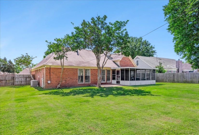 Expansive backyard featuring a brick exterior home with a screened-in patio, mature trees, and a wooden privacy fence