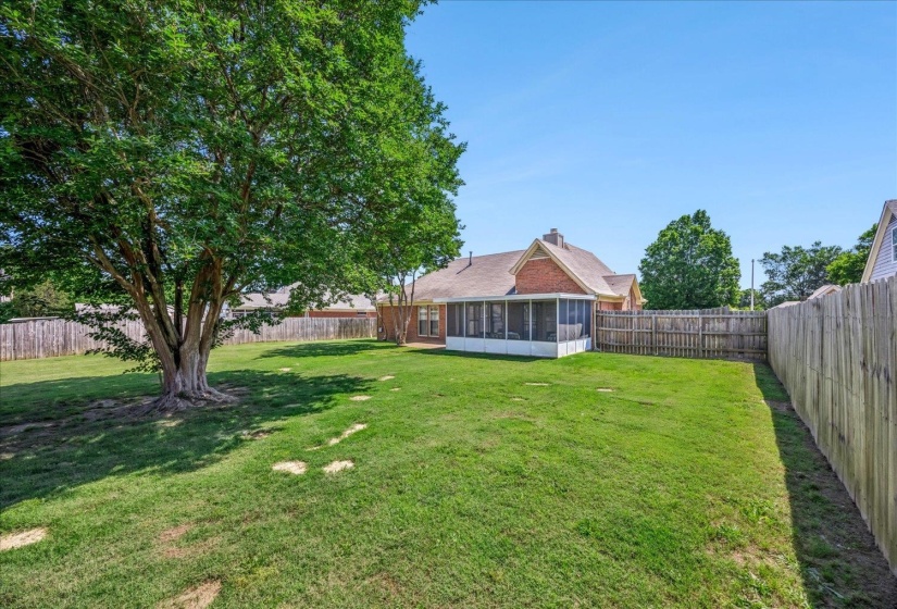 Expansive backyard featuring a large mature tree, manicured lawn, full privacy fencing, and a screened-in porch