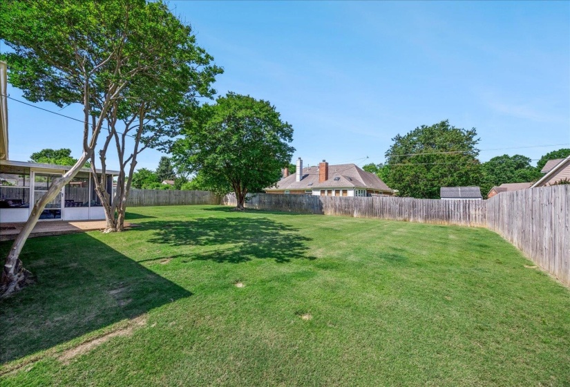 Expansive green lawn with mature trees and a wooden privacy fence