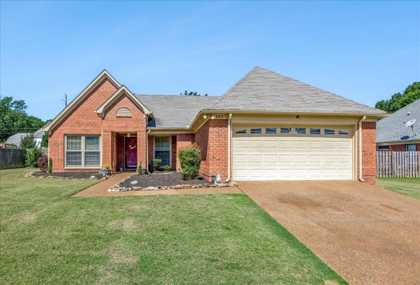 Brick exterior residence featuring a gabled roofline, an attached two-car garage, a gravel driveway, and a front yard with manicured lawn and landscaping
