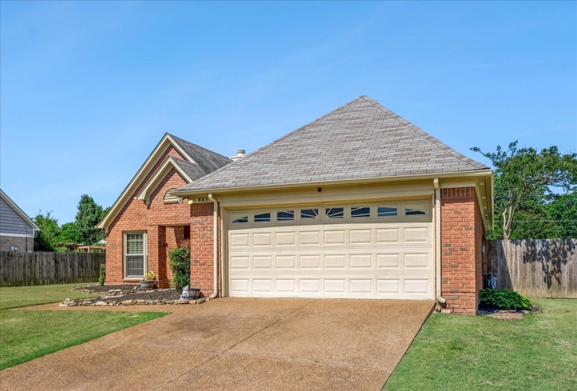 Brick exterior featuring a two-car garage with a panel door, a shingled roof, a paved driveway, and a manicured lawn