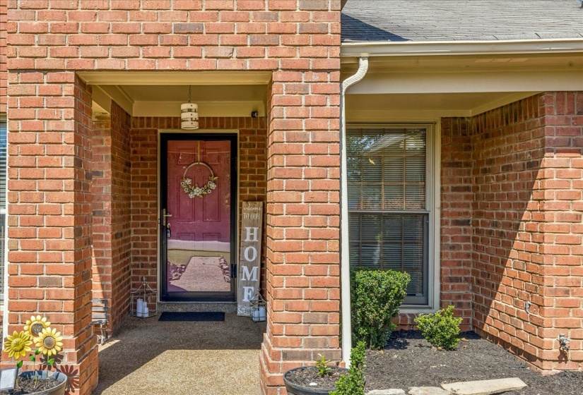 Brick exterior featuring a covered front entry with an overhead light fixture, a storm door, and an adjacent window with blinds
