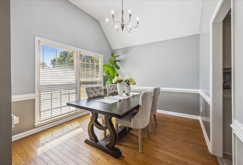 Vaulted ceiling dining area featuring hardwood flooring, a large window with blinds, a chandelier fixture, and two-tone wall paint with wainscoting