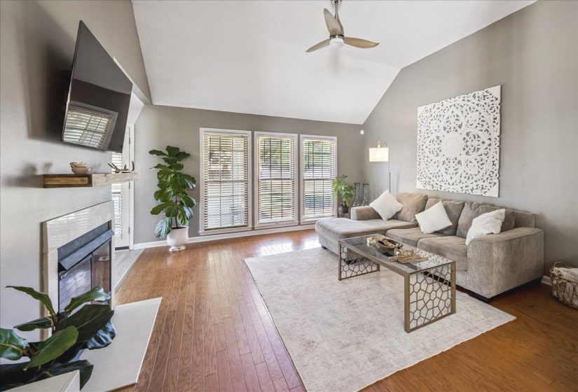 Vaulted ceiling living area featuring wood-finish flooring, a contemporary ceiling fan, and a fireplace with a white tile surround