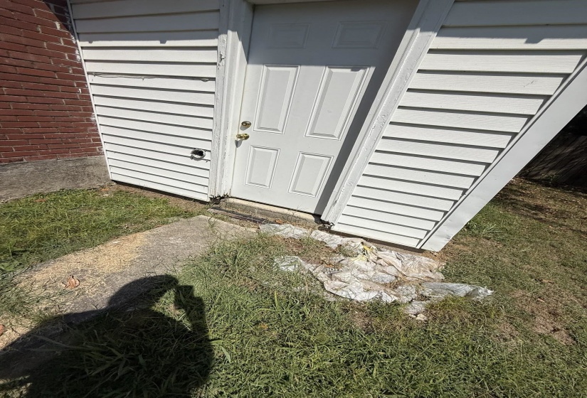 White paneled door with brass hardware, bordered by white horizontal siding and a red brick exterior