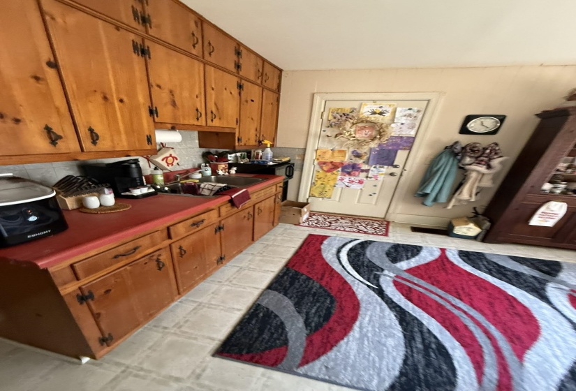 Kitchen featuring extensive wood cabinetry, red countertops, a single basin sink, and neutral tile flooring