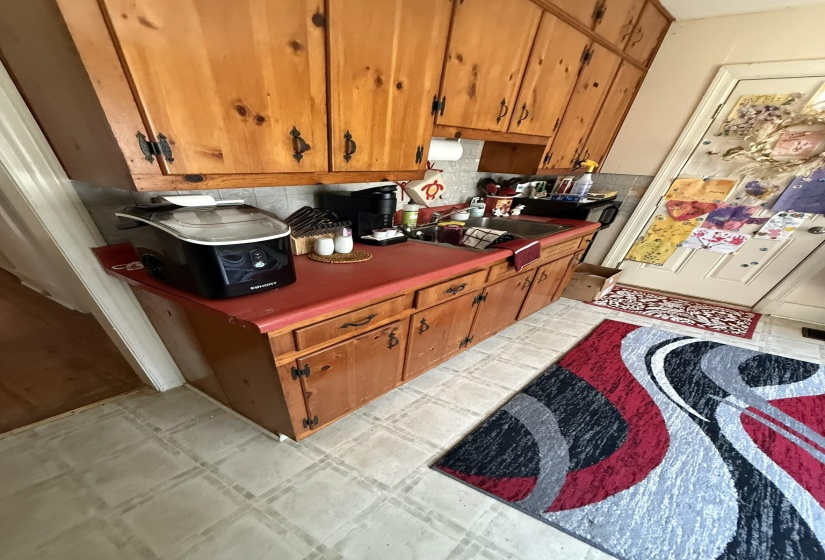 Kitchen featuring wood cabinetry, red countertops, a stainless steel sink, and light-toned vinyl flooring