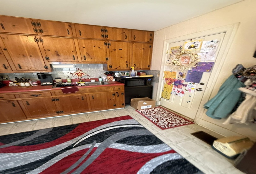 Wood-finish cabinetry with black hardware, red countertops, and a tiled backsplash