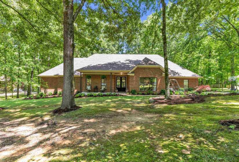 Traditional brick exterior featuring a covered entry, dark-framed double front doors, a pitched roof, and mature tree landscaping