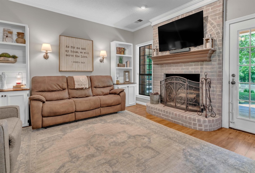 Brick fireplace with a substantial wood mantel, flanked by built-in white shelving and cabinetry