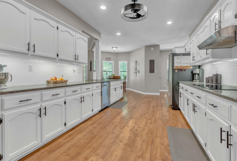 Spacious kitchen featuring extensive white cabinetry, dark countertops, wood-finish flooring, a stainless steel dishwasher, and a range hood
