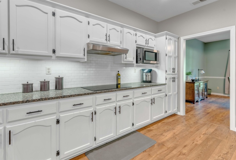 Kitchen featuring white cabinetry with dark hardware, a white subway tile backsplash, and speckled countertops