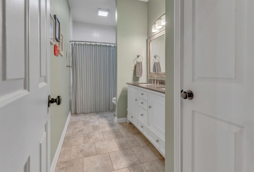 Bathroom featuring a white vanity with integrated sink, a framed mirror with overhead lighting, tiled flooring, and a shower with a privacy curtain