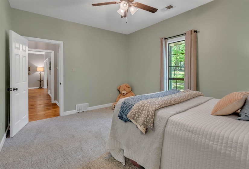 Carpeted bedroom featuring a ceiling fan with integrated lighting, a window with exterior views, and a panel door opening to a hallway with wood-finish flooring
