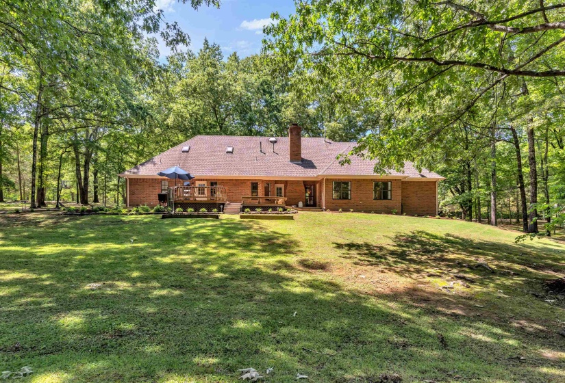 Expansive rear exterior featuring a red brick facade, a multi-level wood deck, and a shingle roof with skylights