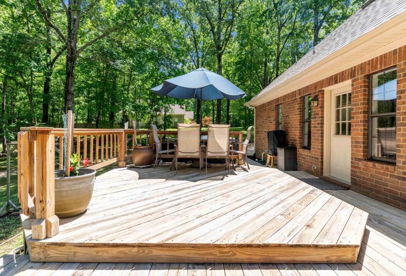 Spacious outdoor deck with natural wood planks, wood railing, and a brick exterior wall