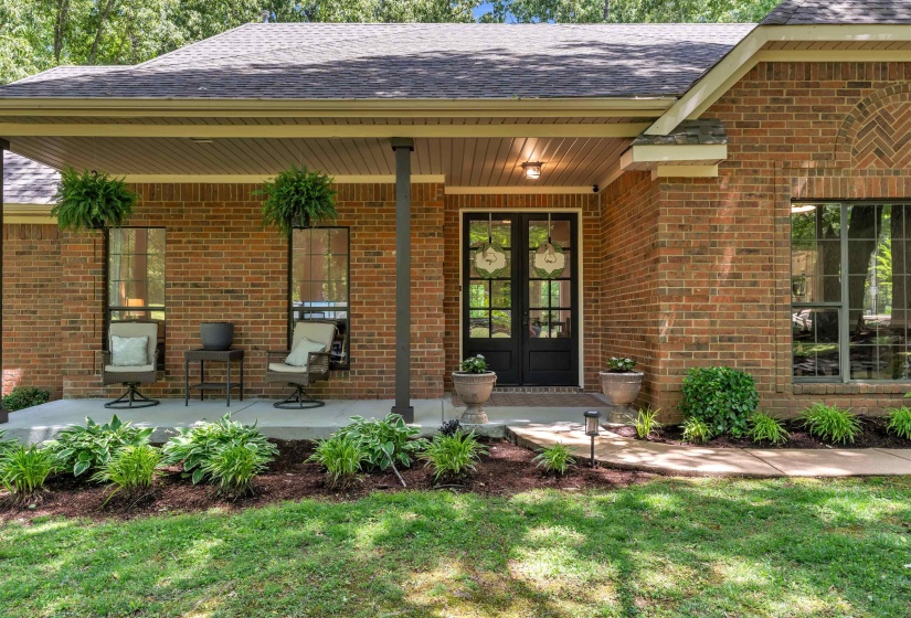 Brick exterior featuring a covered front porch with dark columns, double entry doors with decorative glass panels, and a gabled roofline
