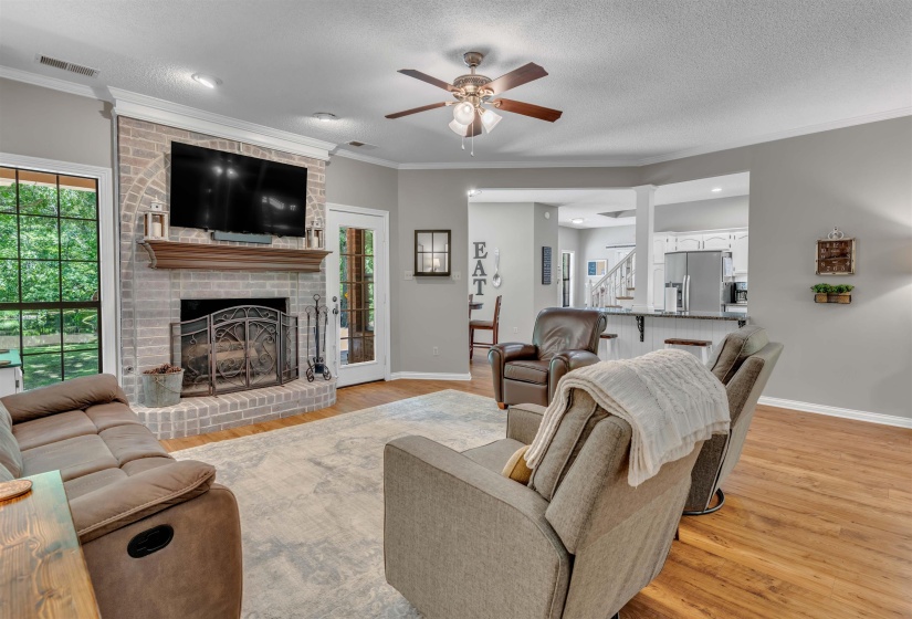 Spacious living area featuring a light-colored brick fireplace with a wood mantel, recessed lighting, crown molding, and wood-finish flooring