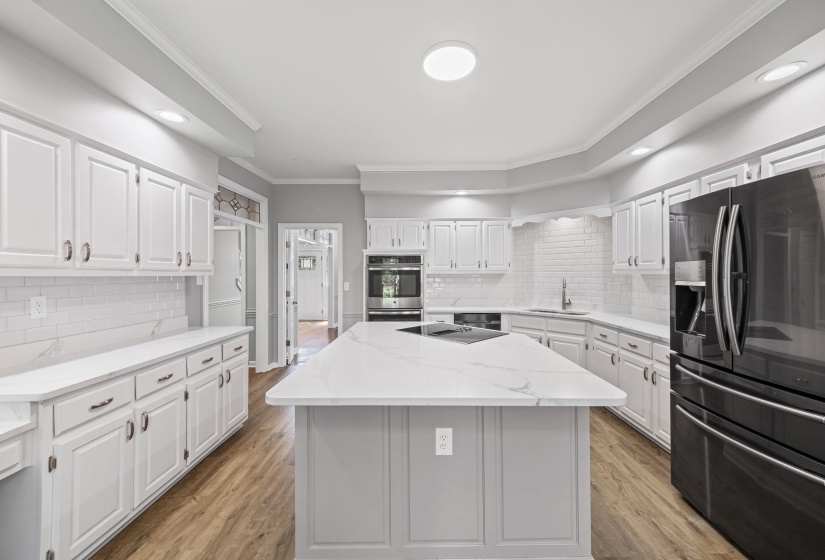 Kitchen featuring crown molding, fridge with ice dispenser, decorative backsplash, light wood finished floors, and white cabinetry