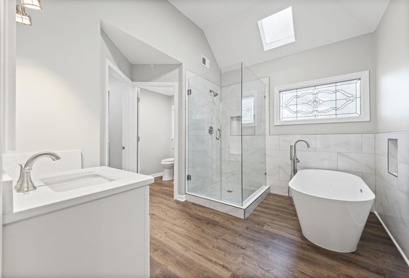 Full bath featuring a skylight, vanity, a soaking tub, a stall shower, and vaulted ceiling