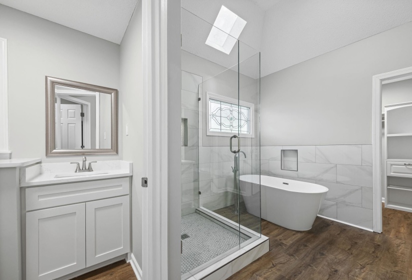 Bathroom with a skylight, a shower stall, vanity, a freestanding bath, and dark wood finished floors