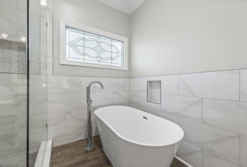 Bathroom with tile walls, a soaking tub, wainscoting, dark wood-type flooring, and a tile shower
