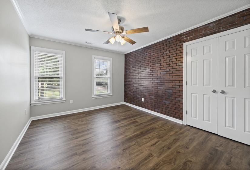 Unfurnished bedroom with brick wall, crown molding, a textured ceiling, a closet, and dark wood-type flooring
