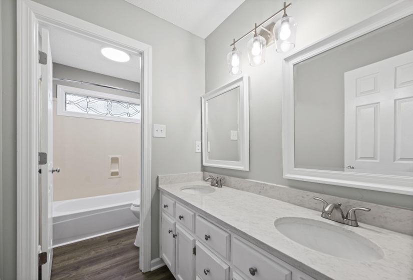 Full bath featuring double vanity, dark wood-style floors, and shower / bath combination
